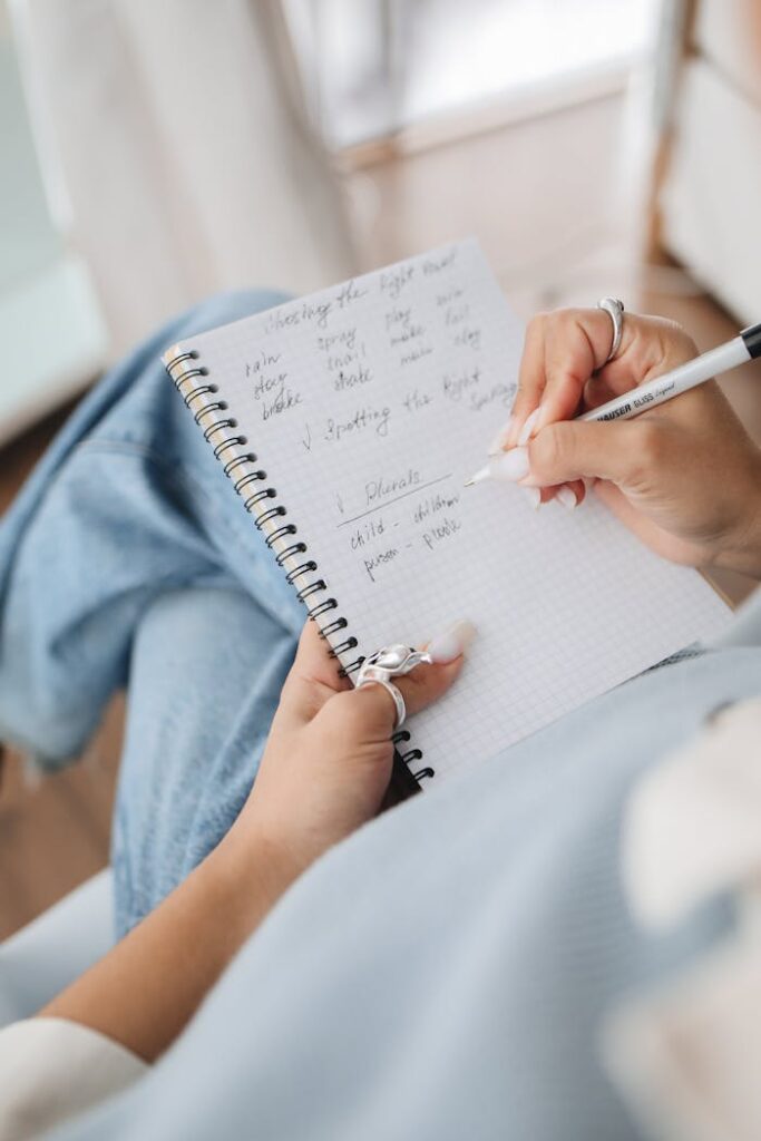 Close-up of a woman writing thoughts in a spiral notebook, focusing on handwriting and personal reflection.